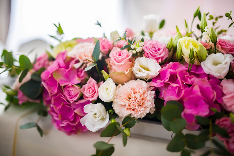 A floral arrangement featuring a variety of fresh flowers including pink roses, white lisianthus, pale peach carnations, and light yellow eustoma, elegantly arranged with green eucalyptus leaves. The
